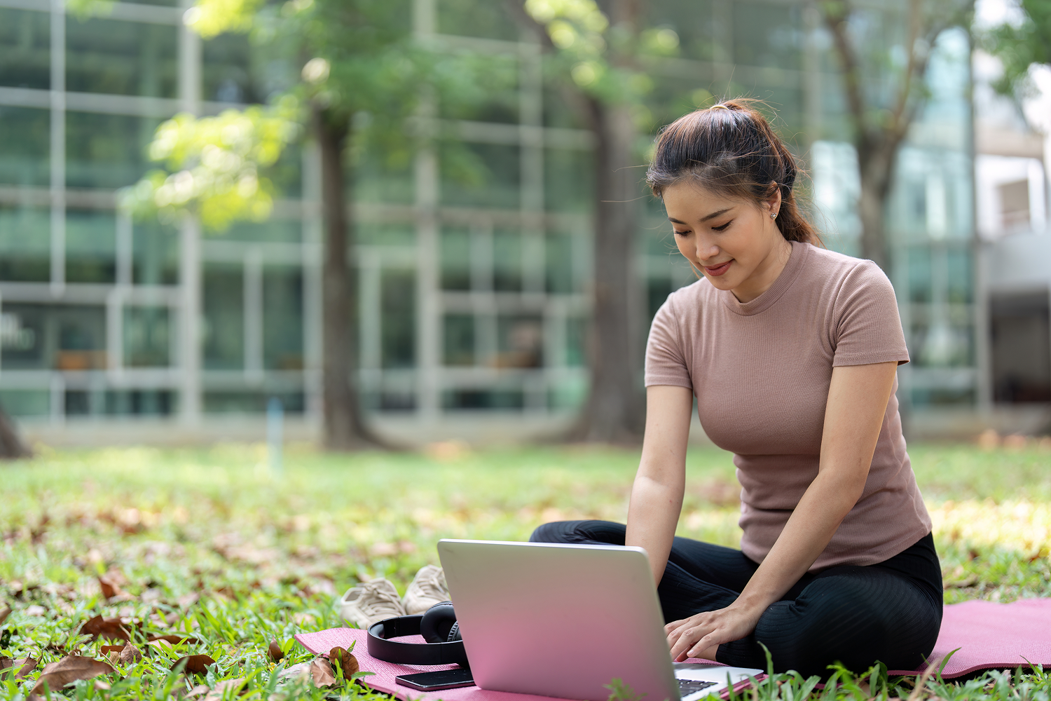 Woman sitting on park grass using laptop
