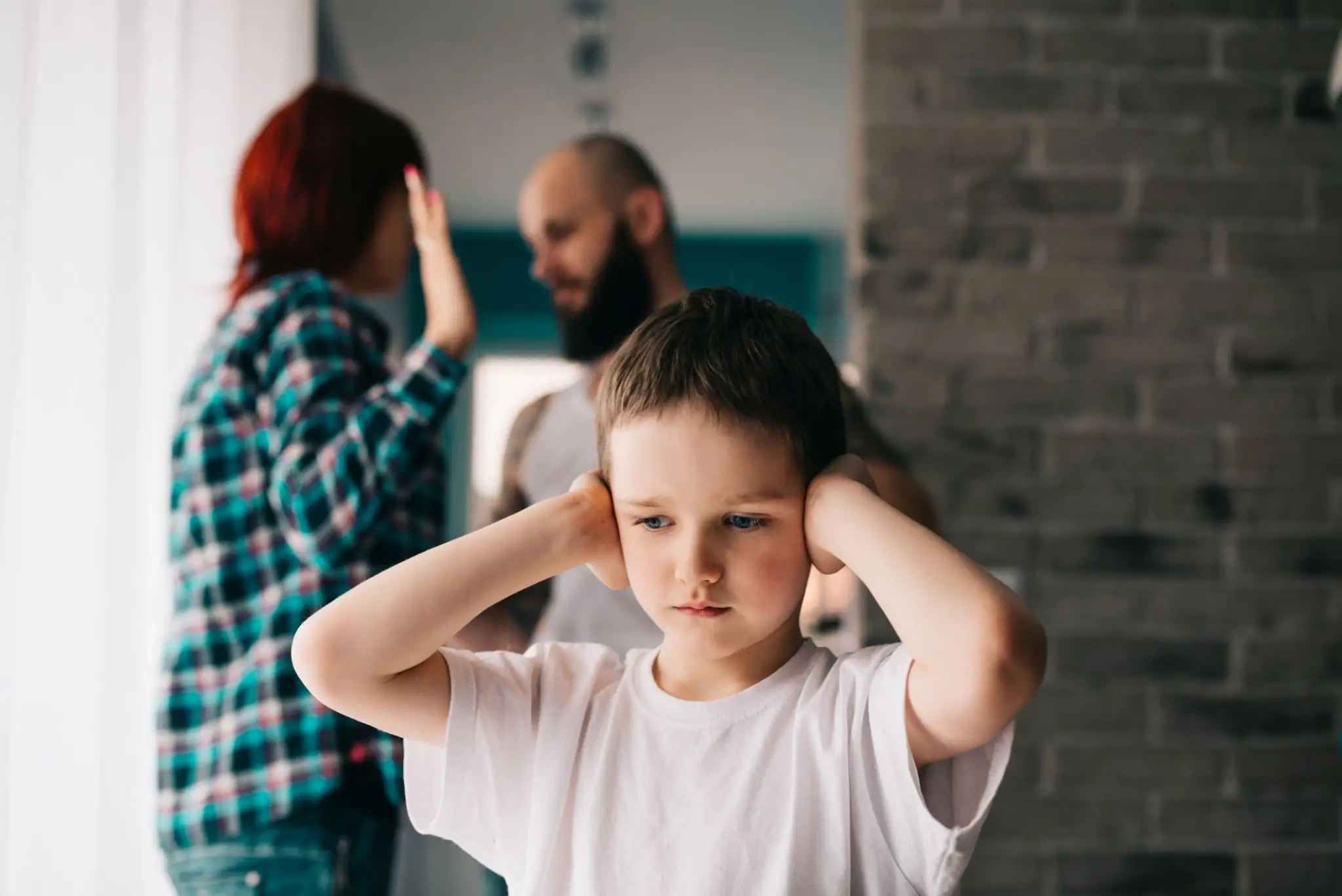 Child covering ears while parents argue in background