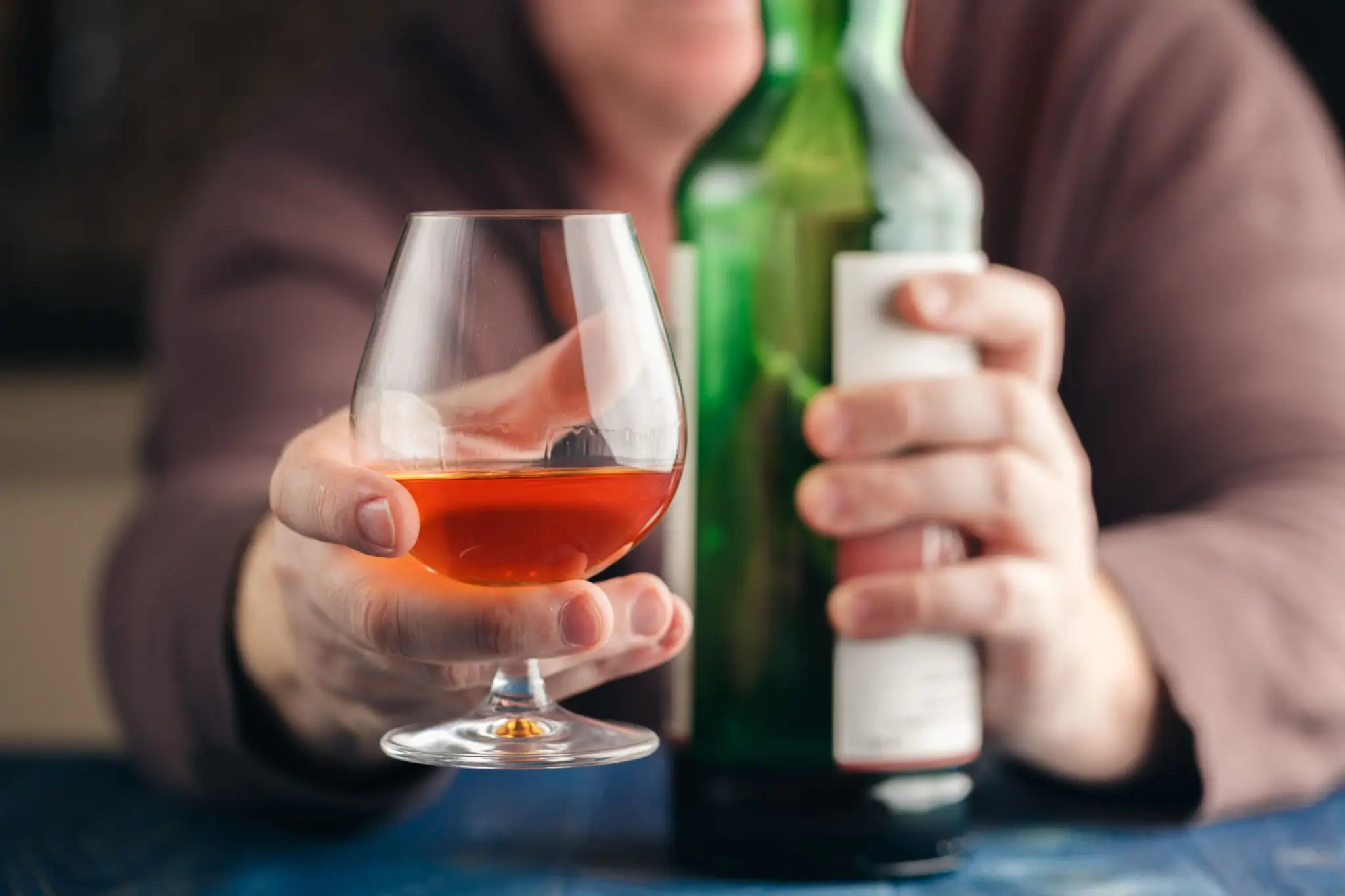 Hand holding brandy glass and green bottle
