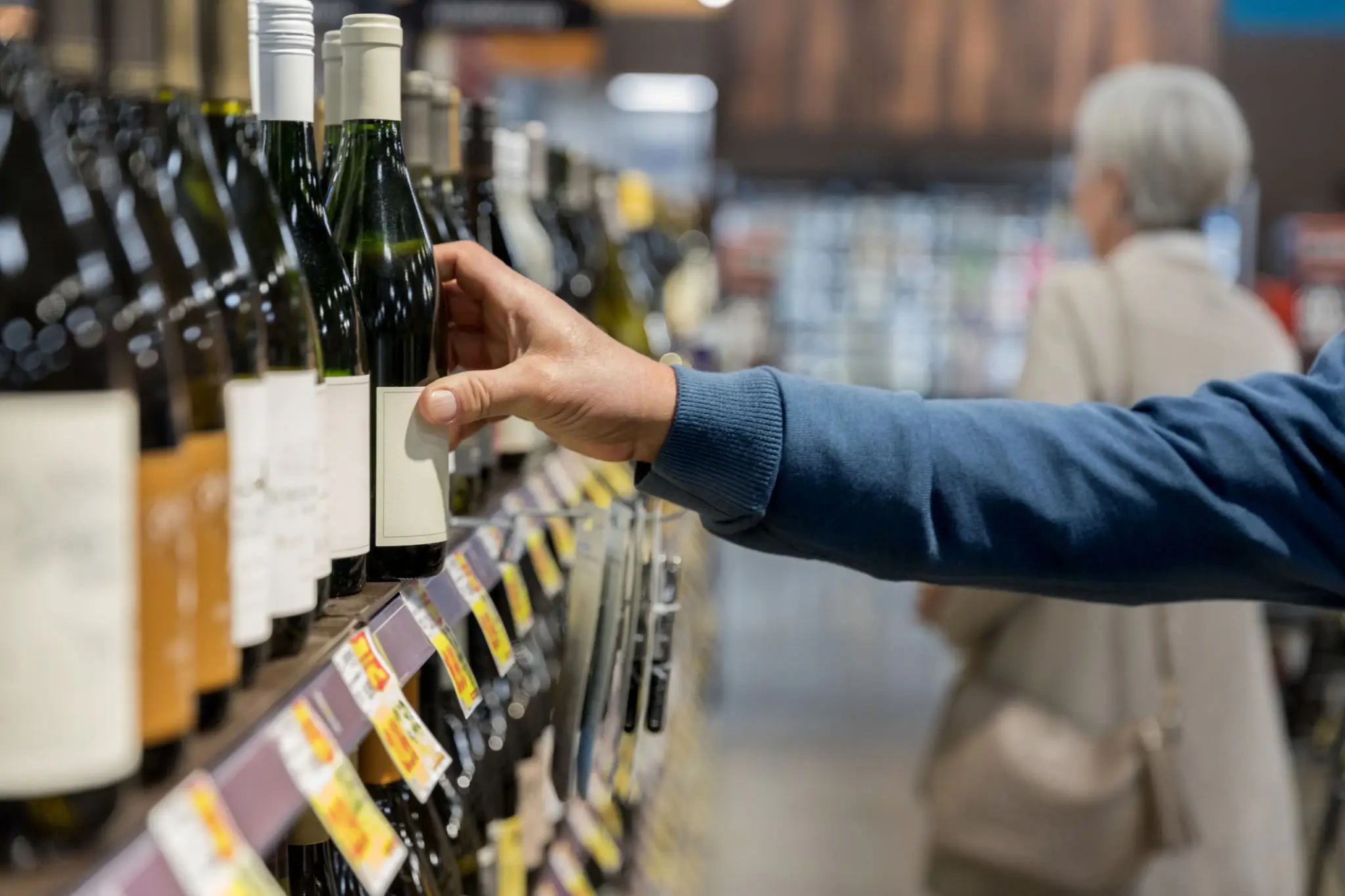 Hand reaching for wine bottle on store shelf