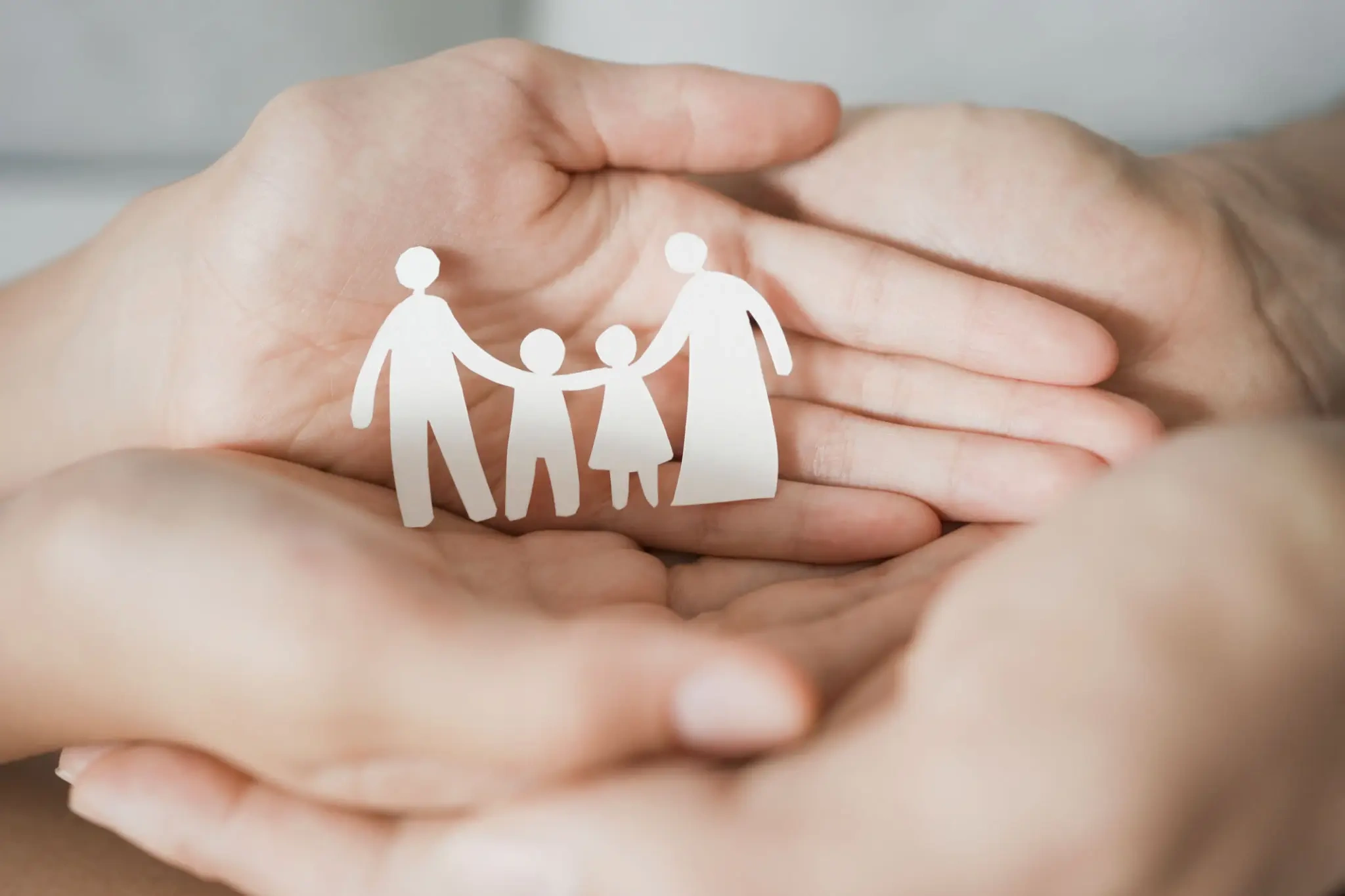 Cupped hands holding paper cutout family figures