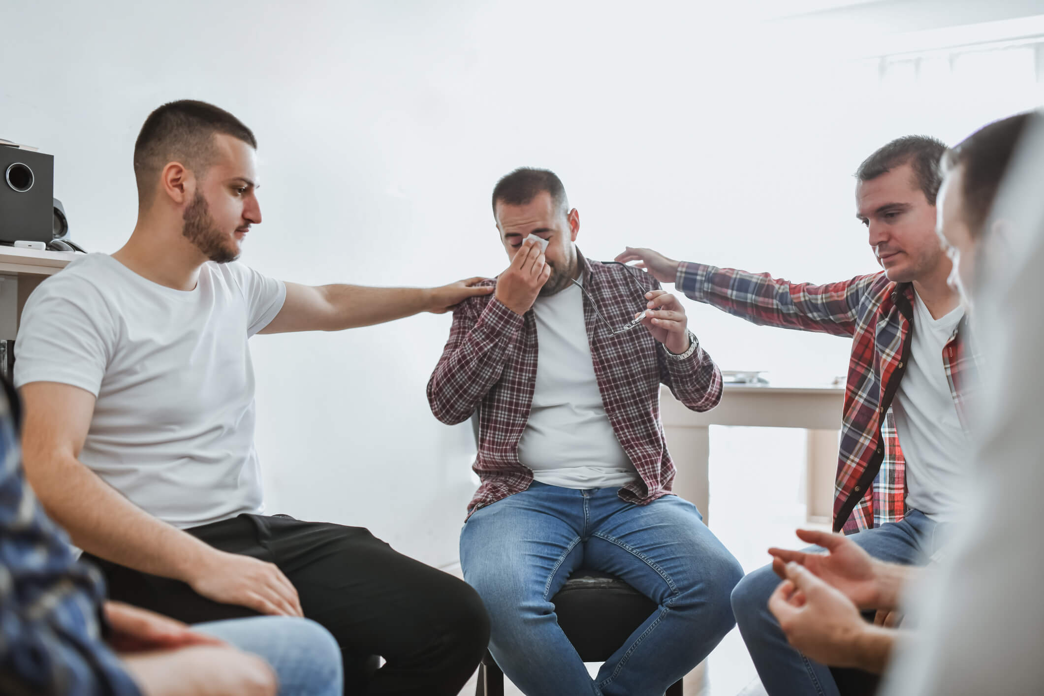 Men consoling crying man in support group